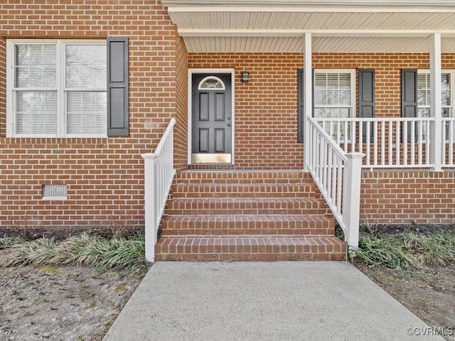 view of exterior entry with covered porch, brick siding, and crawl space