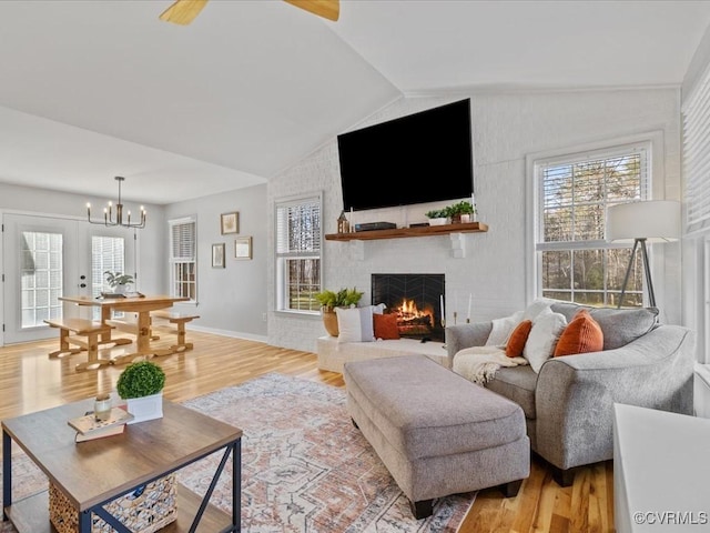 living room with light wood-style floors, lofted ceiling, a brick fireplace, and an inviting chandelier