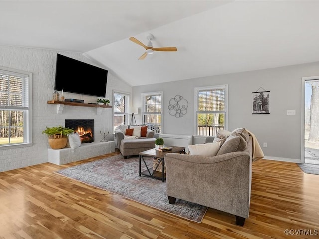 living room with a wealth of natural light, vaulted ceiling, a fireplace, and wood finished floors