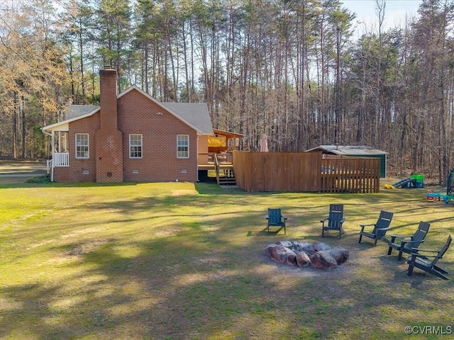 view of yard with a forest view, an outdoor fire pit, and a wooden deck