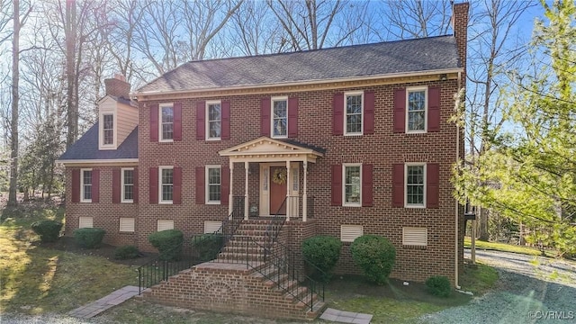 georgian-style home with crawl space, brick siding, a chimney, and roof with shingles