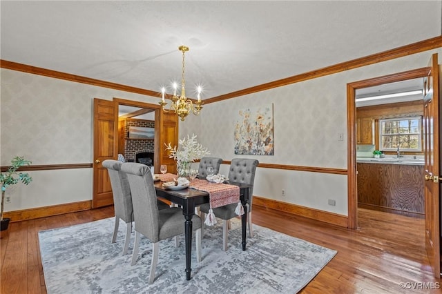 dining room with a notable chandelier, baseboards, a brick fireplace, hardwood / wood-style floors, and wallpapered walls