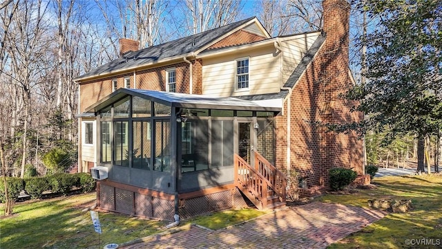 rear view of property with a sunroom, a chimney, a lawn, and brick siding