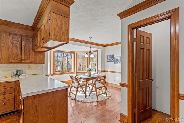 kitchen featuring brown cabinets, light countertops, ornamental molding, a textured ceiling, and hardwood / wood-style flooring