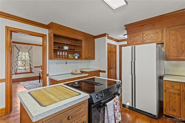 kitchen with brown cabinets, wood finished floors, freestanding refrigerator, black / electric stove, and light countertops