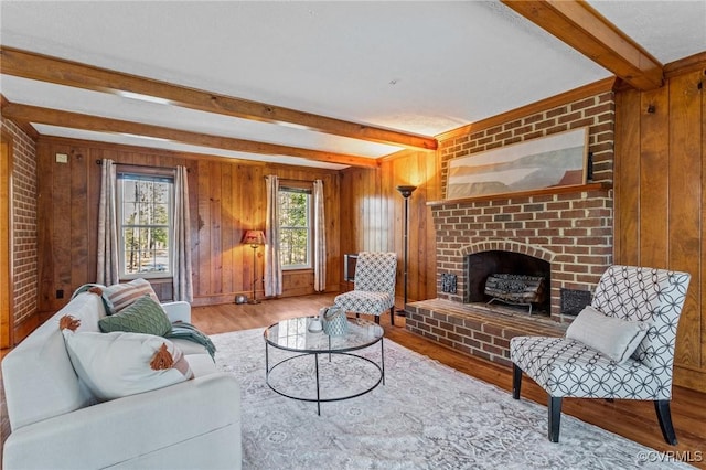 living room featuring a fireplace, beamed ceiling, wood walls, and wood finished floors