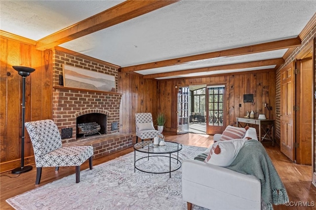 living area with wooden walls, beamed ceiling, wood finished floors, a textured ceiling, and a brick fireplace