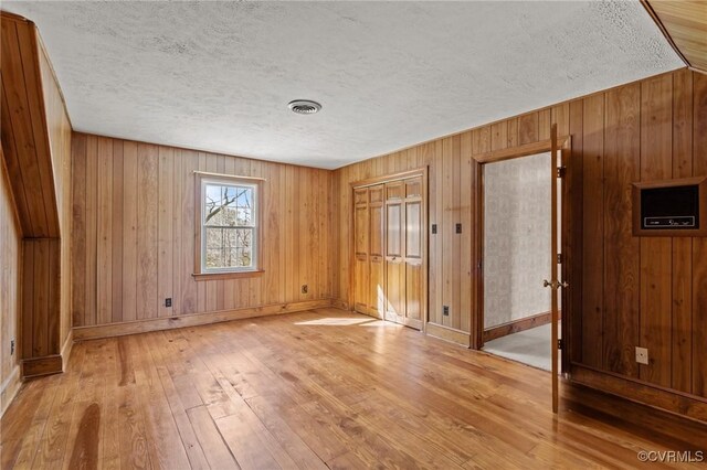 unfurnished room with a textured ceiling, hardwood / wood-style flooring, wooden walls, visible vents, and baseboards