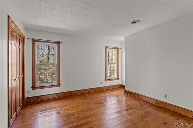 empty room featuring a textured ceiling, visible vents, and hardwood / wood-style floors