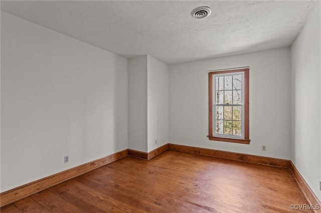 empty room with baseboards, visible vents, a textured ceiling, and hardwood / wood-style floors