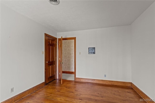 empty room featuring baseboards, visible vents, and wood finished floors