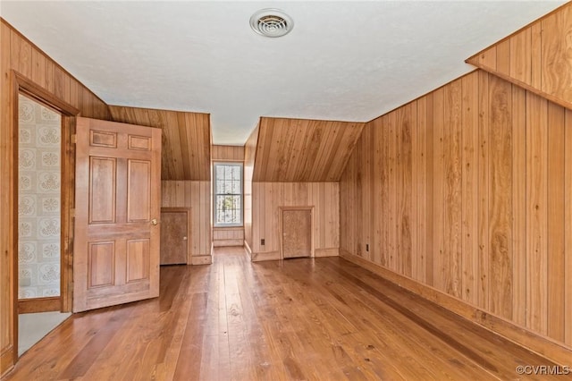 bonus room with hardwood / wood-style flooring, visible vents, and wooden walls