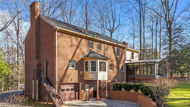 view of front of home with brick siding, a chimney, stairway, an attached garage, and a sunroom