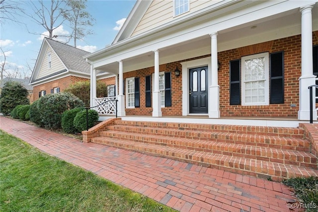 doorway to property with covered porch and brick siding