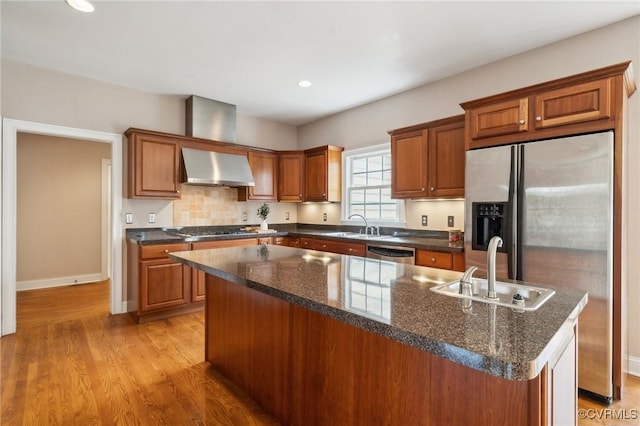 kitchen featuring a sink, wall chimney range hood, appliances with stainless steel finishes, a center island, and brown cabinetry