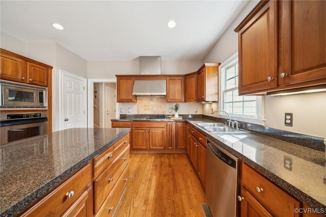 kitchen with stainless steel appliances, wall chimney exhaust hood, a sink, and brown cabinetry