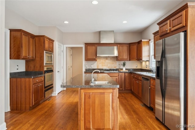 kitchen featuring appliances with stainless steel finishes, a kitchen island with sink, a sink, and light wood-style flooring