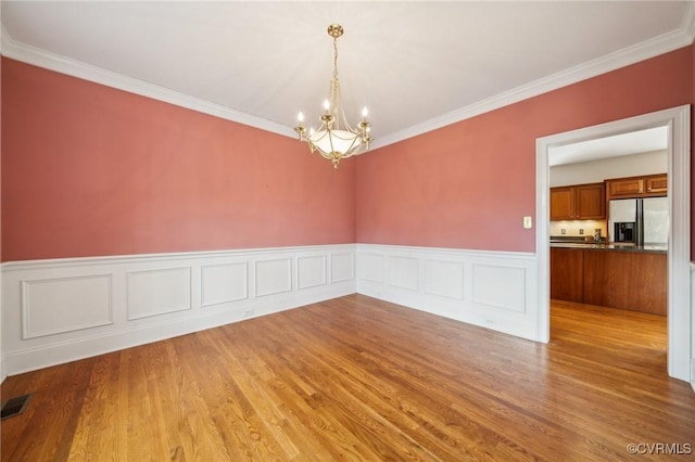 spare room with crown molding, wood finished floors, visible vents, and a notable chandelier