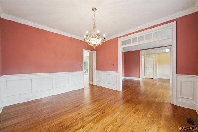 unfurnished room featuring a wainscoted wall, visible vents, an inviting chandelier, ornamental molding, and wood finished floors