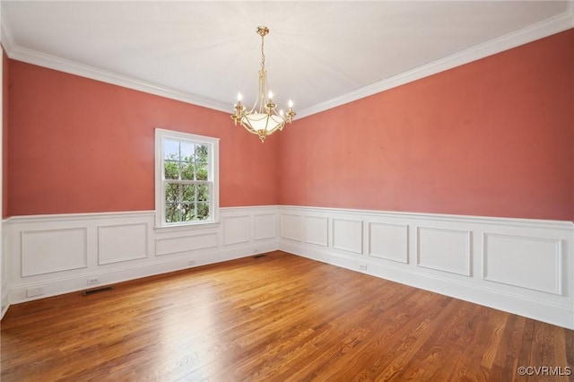 empty room featuring ornamental molding, wood finished floors, visible vents, and an inviting chandelier