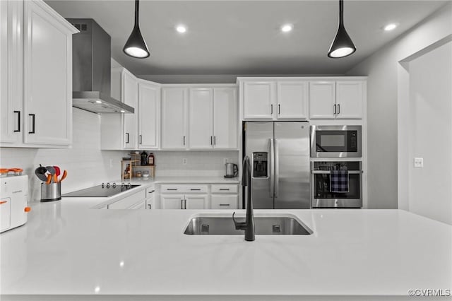 kitchen with wall chimney exhaust hood, appliances with stainless steel finishes, a sink, and white cabinetry