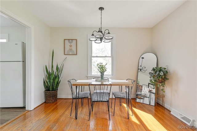 dining space with a chandelier, light wood finished floors, visible vents, and baseboards