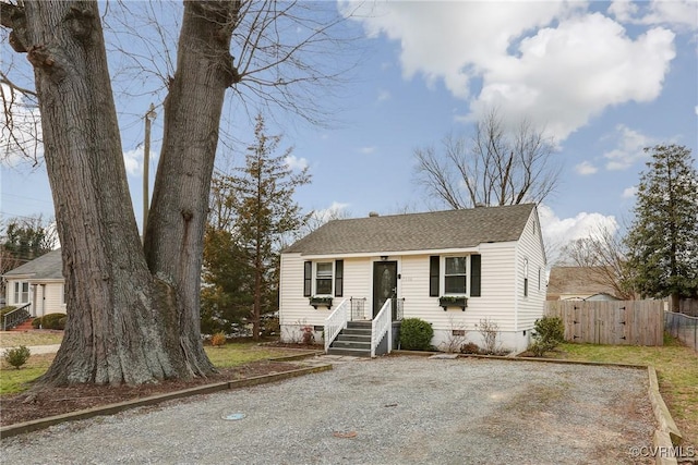 view of front facade with driveway, roof with shingles, and fence