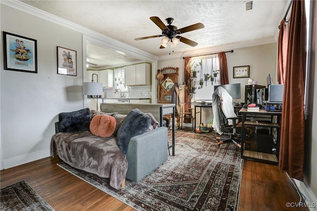 living area with a textured ceiling, wood finished floors, a ceiling fan, visible vents, and crown molding