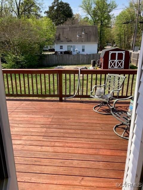 wooden terrace with a fenced backyard, an outdoor structure, a shed, and a lawn
