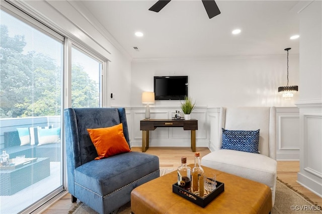 living area featuring a wainscoted wall, light wood-style floors, a ceiling fan, and a decorative wall