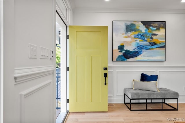 entrance foyer with light wood-style flooring, a decorative wall, a wainscoted wall, visible vents, and ornamental molding