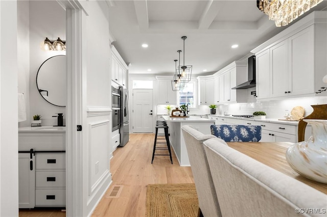 kitchen featuring light wood finished floors, wall chimney exhaust hood, a breakfast bar area, white cabinetry, and a sink