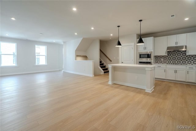 kitchen with wall oven, stainless steel microwave, light wood-type flooring, under cabinet range hood, and backsplash