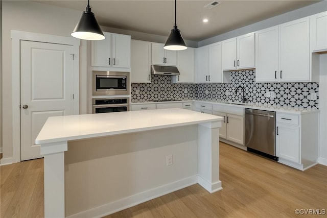 kitchen with under cabinet range hood, a sink, appliances with stainless steel finishes, light wood-type flooring, and backsplash