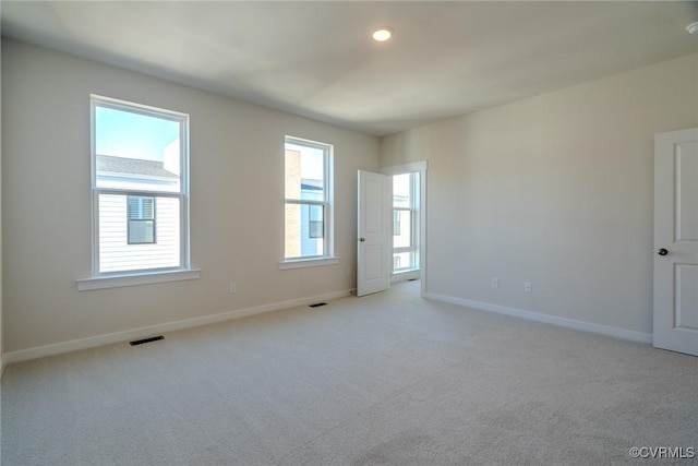 empty room with light colored carpet, a healthy amount of sunlight, visible vents, and baseboards