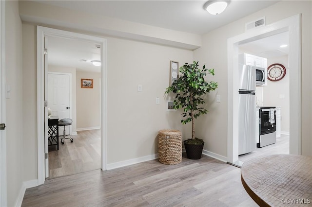 hallway with baseboards, visible vents, and light wood-style floors