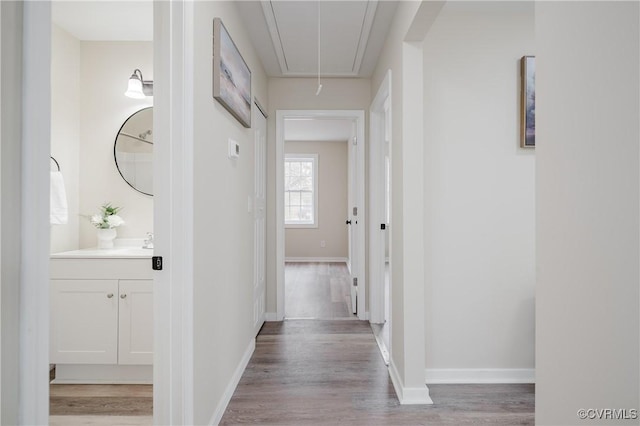 hall with attic access, a sink, light wood-style floors, and baseboards