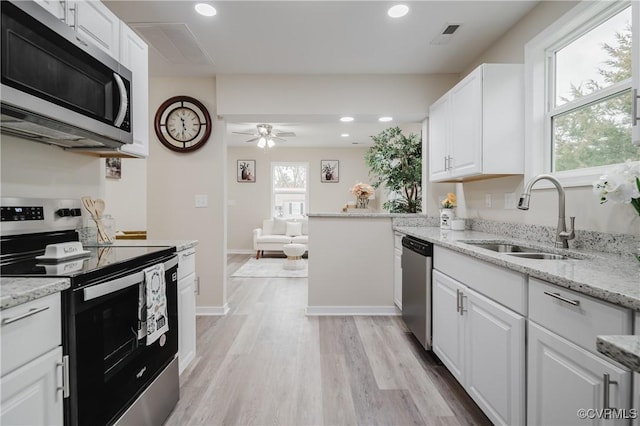 kitchen with stainless steel appliances, a sink, white cabinetry, light wood-type flooring, and light stone countertops