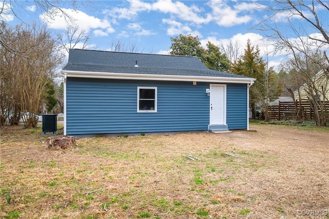 back of property with central air condition unit, roof with shingles, and a yard