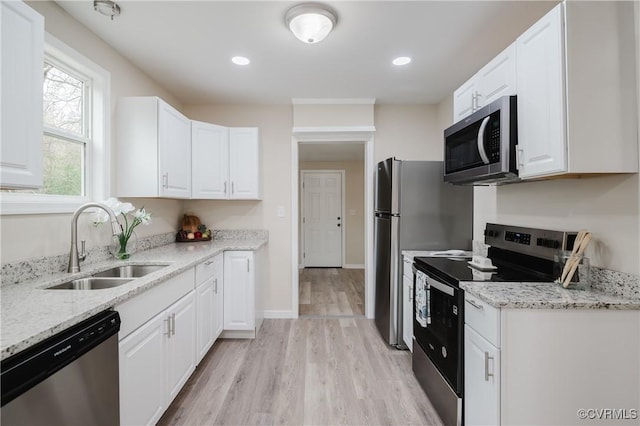 kitchen with light stone counters, white cabinetry, stainless steel appliances, and a sink