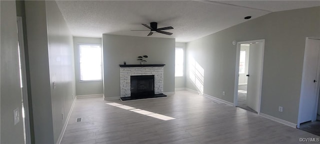 unfurnished living room with a brick fireplace, a textured ceiling, visible vents, and wood finished floors