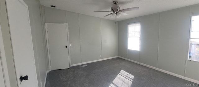 empty room with ceiling fan and dark colored carpet