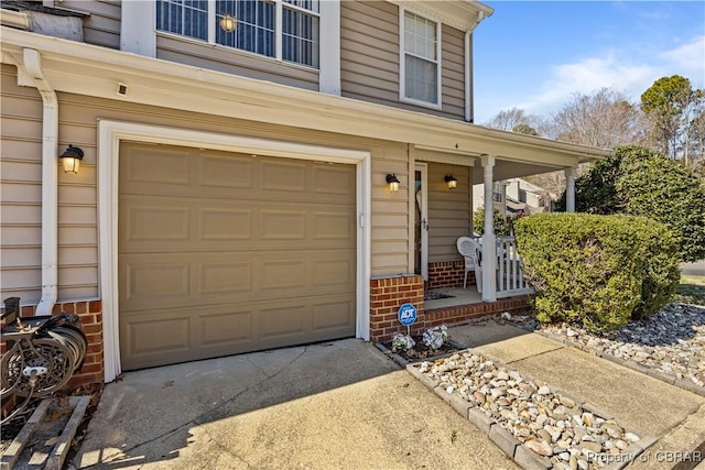 view of exterior entry with an attached garage, a porch, concrete driveway, and brick siding