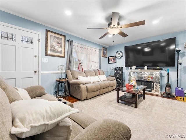 living area featuring a glass covered fireplace, ornamental molding, wood finished floors, and a ceiling fan