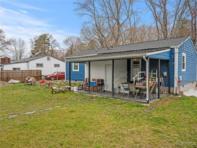 rear view of house featuring roof with shingles, a yard, crawl space, a patio area, and fence