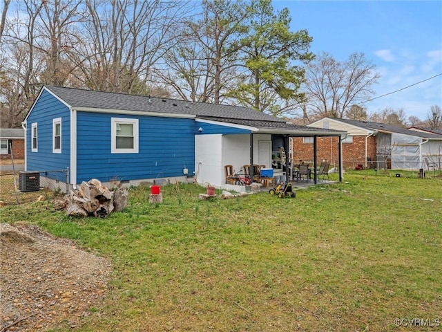 rear view of house with a patio, central AC, fence, roof with shingles, and a lawn