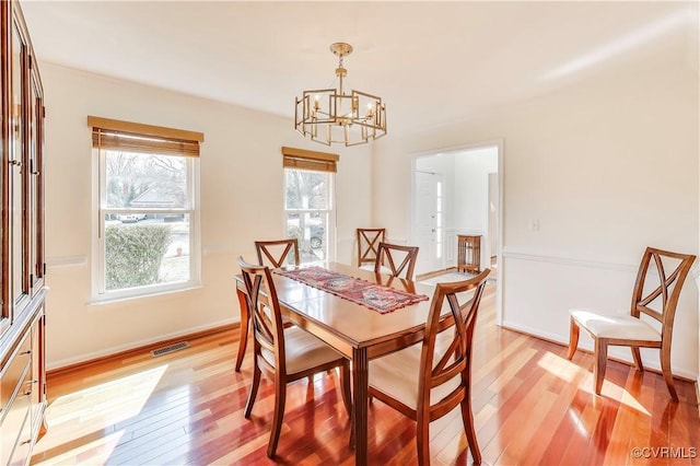 dining room with baseboards, light wood finished floors, visible vents, and an inviting chandelier