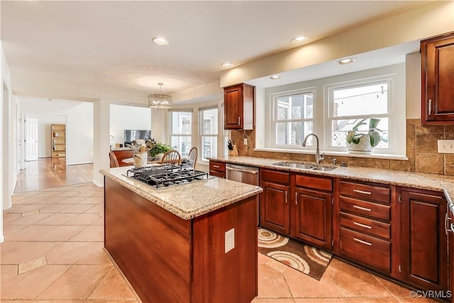 kitchen with light stone counters, appliances with stainless steel finishes, a center island, a sink, and backsplash