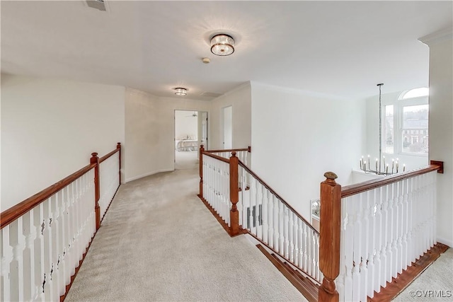 hall featuring carpet floors, a chandelier, and an upstairs landing