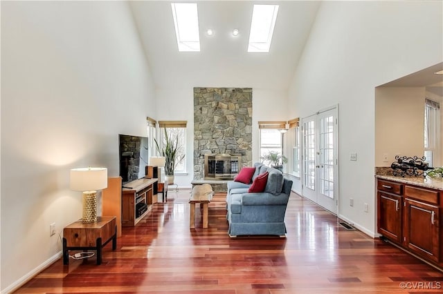 living area with a healthy amount of sunlight, dark wood-type flooring, a stone fireplace, and french doors